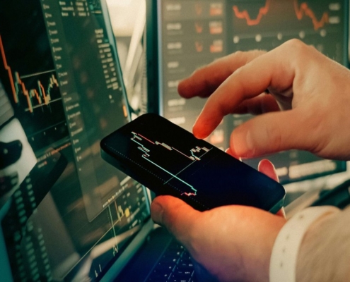 스마트폰으로 실시간 주식 시장 그래프와 경제 데이터를 분석하고 있는 전문가의 손과 사무실 배경
