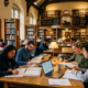 Group of students studying around a table with books, notes, and laptops in a library.