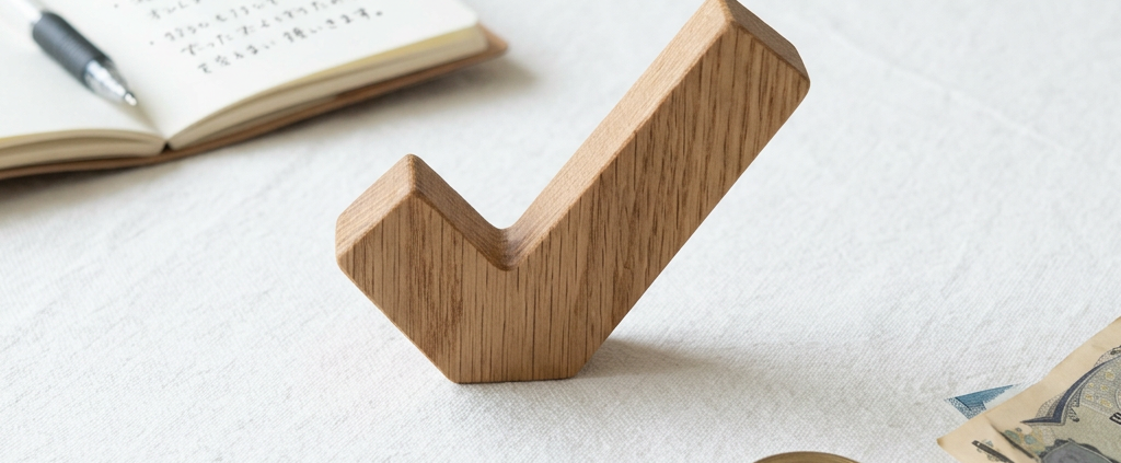 Wooden checkmark symbol on a white tablecloth near coins, Japanese yen bills, and an open notebook with handwritten notes.